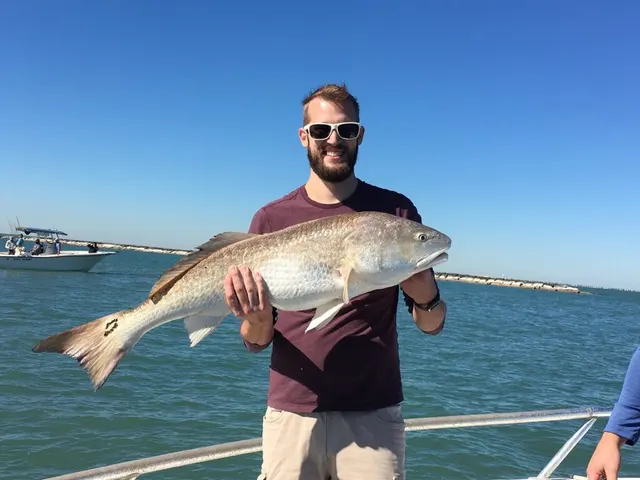 Angler with a bull redfish on the deck, calm Galveston water behind